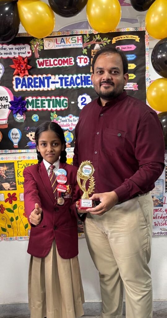 A student topper in school uniform receives her trophy at Parent Teacher Meeting 2, LAKSH Vijaynagar Colony